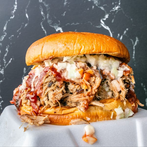 Willie's Famous pulled pork sandwich with coleslaw and BBQ sauce on a bun, in a takeout container.