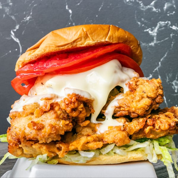 Willie's Famous crispy chicken sandwich with melted cheese, tomato, and lettuce on a bun.